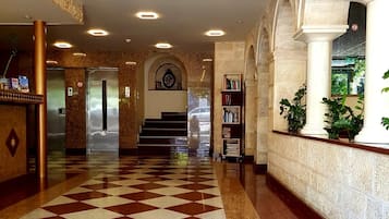 Un vestíbulo de hotel con piso a cuadros, una recepción, una escalera y una estantería.