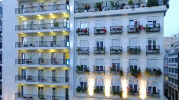 Un hotel de varios pisos con balcones, un letrero que dice 'POSSEUDO ONTO' y una entrada bien iluminada.