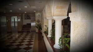 Un hall d’entrée avec un sol à carreaux, des colonnes et des plantes en pot.