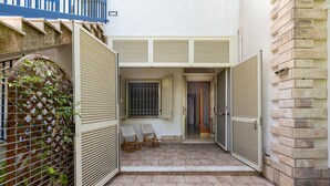 Un patio con piso de baldosas, dos sillas, una reja y un muro con diseño de celosía.
