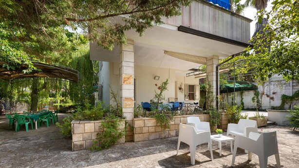 Un patio al aire libre con suelo de piedra, mobiliario de plástico blanco y verde y plantas en macetas.