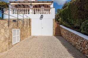 A gated entrance with a stone wall, a metal staircase, and a white door. - V105 | Villa S'Illot (Torre Soli Nou)