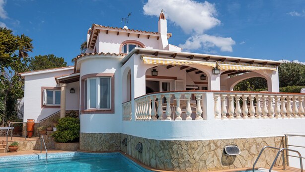 Une maison à deux étages avec une piscine, un mur en pierre et un balcon doté d’une balustrade.