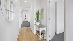 Un couloir avec un plancher en bois, des murs blancs, un miroir rond, une plante en pot et une citation encadrée accrochée au mur.