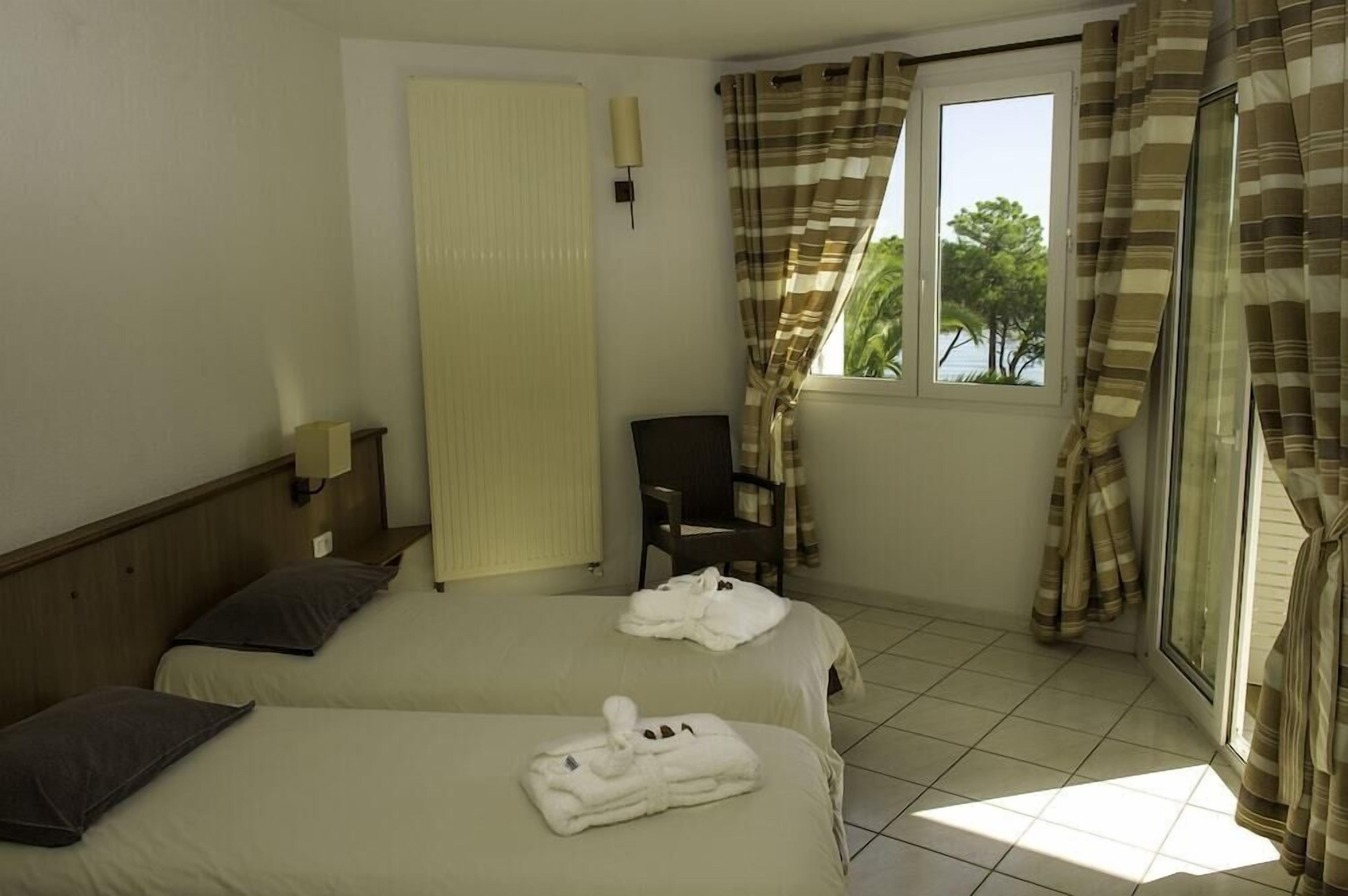 Une chambre d’hôtel avec deux lits, une chaise, une fenêtre avec des rideaux et une vue sur la verdure.