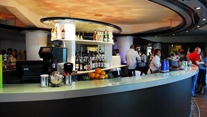 Un espace bar doté d’un comptoir incurvé, d’étagères remplies de bouteilles et d’un plafond au motif ondulé.
