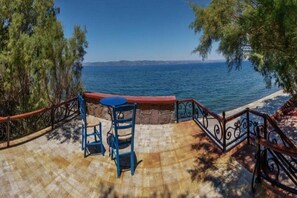 A terrace with a stone floor, two blue chairs, and a small round table. - Olive Grove (Lesvos)