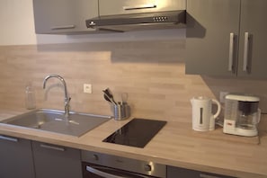 A modern kitchen with a stainless steel sink, an induction cooktop, a coffee maker, and a kettle.