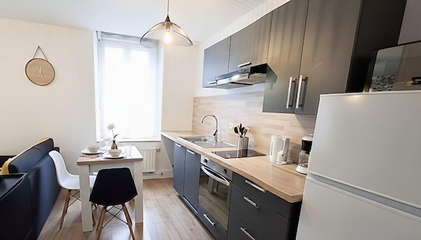 A modern kitchen with a sink, stove, and refrigerator, a dining table with chairs, and a window providing natural light.