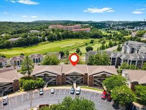 Ein mehrstöckiges Hotel mit Parkplatz, umgeben von viel Grün und einem Golfplatz.