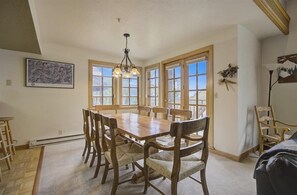 Un espace repas avec une table et des chaises en bois, de grandes fenêtres et un lustre.