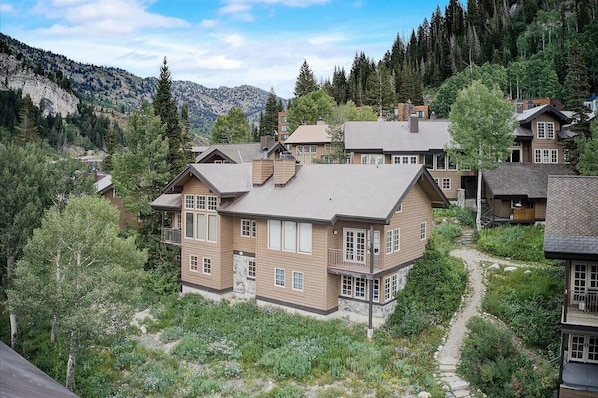 Ein mehrgeschossiges Haus mit Steinfundament, umgeben von üppigem Grün und einer Bergkulisse.