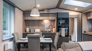 A modern kitchen with a dining area, featuring a table set for four, a sofa, and a ceiling light. - Luxury Lodge in Stunning Surroundings (York)
