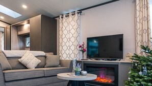 A modern living room with a grey sofa, a flat-screen TV, a fireplace, and a Christmas tree. - Luxury Lodge in Stunning Surroundings (York)