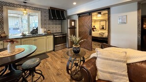 A compact kitchen with a dining area, a living room with a sofa, and a bedroom visible through an open door. - Camelot on Lake Hamilton | Dock, Hot Tub + Theater (Hot Springs)