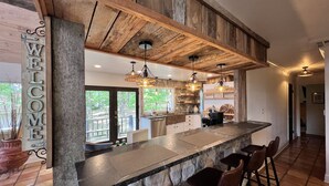 A rustic kitchen with a stone countertop, wooden beams, and a 'WELCOME' sign. - Camelot on Lake Hamilton | Dock, Hot Tub + Theater (Hot Springs)