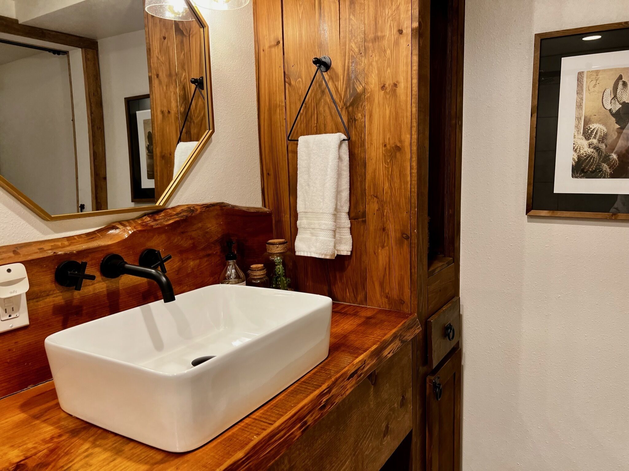 Ein Badezimmer mit einem weißen Waschbecken, einer Holzkommode, einem Spiegel und einem gerahmten Bild an der Wand.