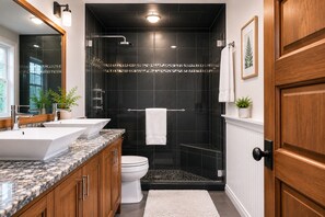 A modern bathroom with two sinks, a toilet, a shower, and a wooden door.