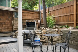 An outdoor patio with a grill, two metal chairs, a table, and a stone wall. - Après Ski Retreat at Voss Ski Haus 949 (Park City)