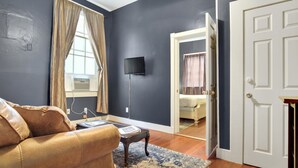 Una habitación con un sofá de cuero marrón, una mesita de madera, una alfombra estampada, un televisor de pantalla plana montado en la pared y una puerta que da a otra estancia.