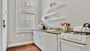 Una cocina con armarios blancos, estufa, microondas y ventana con diseño de ladrillo.
