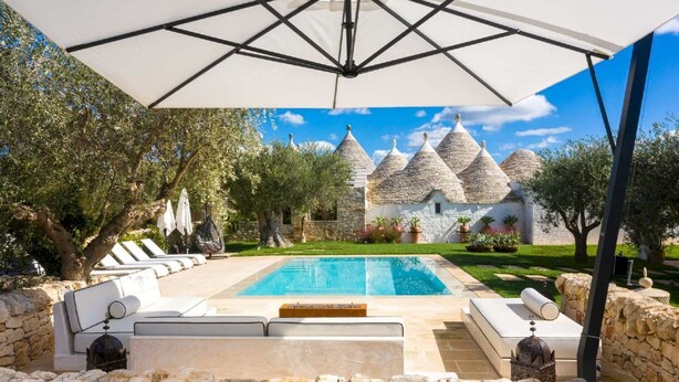 A pool area with stone walls, outdoor seating, and a view of traditional stone buildings in the background.