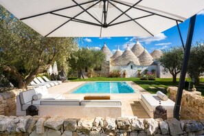 A pool area with stone walls, outdoor seating, and a view of traditional stone buildings in the background. - Trullo Ermes - Luxury trullo with private pool, garden and exclusive design (Martina Franca)