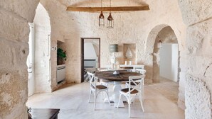 A rustic dining area with a round wooden table, white chairs, and a stone wall backdrop.