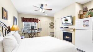 Habitación de hotel con cama, escritorio con silla, televisor, chimenea y ventilador de techo.