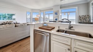 A modern kitchen with a built-in dishwasher, a large window, and a view of the ocean.