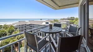 A balcony with a table and chairs overlooking a beach and ocean.