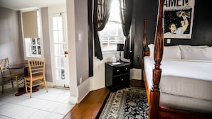Une chambre à coucher avec un lit, une table de chevet, une commode, une chaise, une fenêtre avec des rideaux et une affiche accrochée au mur.