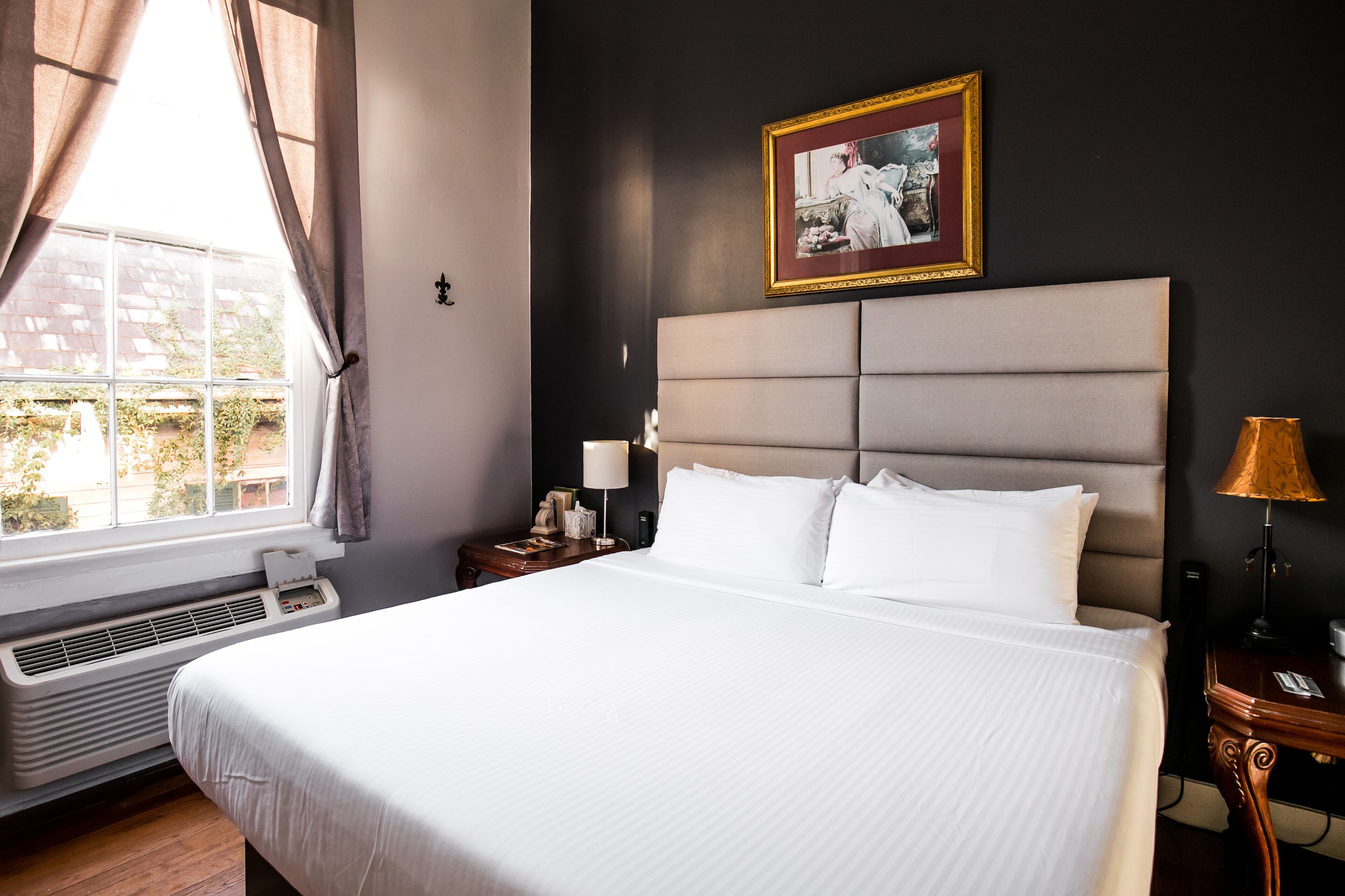 Une chambre d’hôtel avec un grand lit, une table de chevet avec une lampe, un tableau accroché au mur et une fenêtre avec des rideaux.