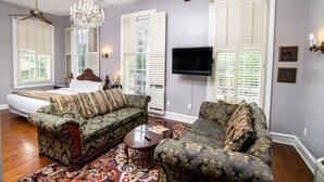 A room with a bed, two sofas, a chandelier, a ceiling fan, and a TV.