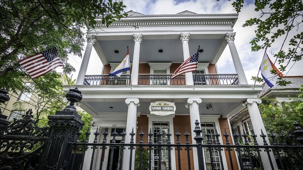 A historic building with a balcony, columns, and flags.