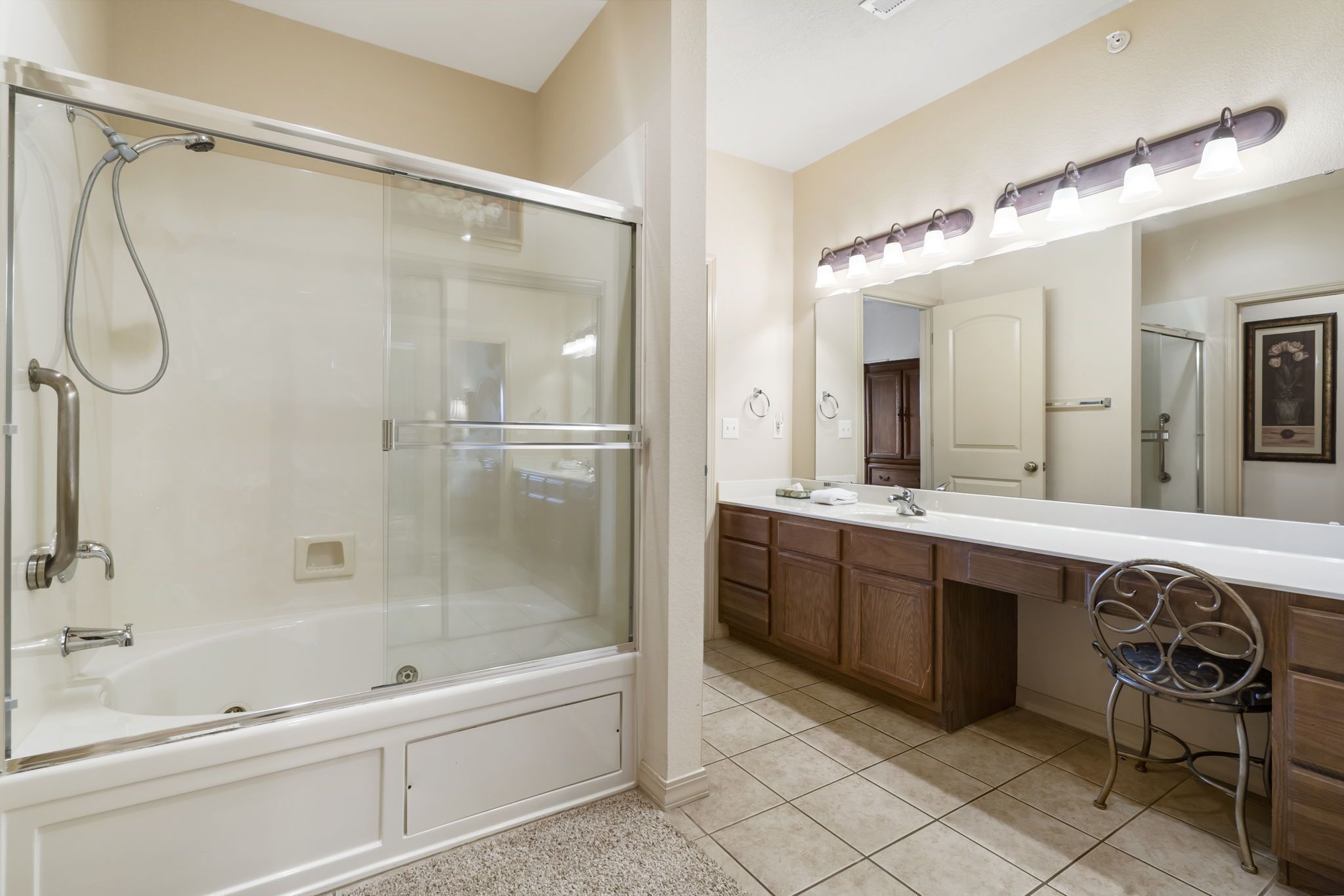 A bathroom with a glass-enclosed shower, a vanity with a mirror and lights, and wooden cabinets.