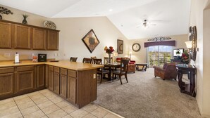 A spacious kitchen with wooden cabinets, a dining area with a table and chairs, and a living room with a sofa and a TV. - 2 King BR, 2BA Golf Condo - Private Balcony with View (Branson)