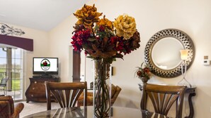 A dining table with a vase of flowers, wooden chairs, a television, and a decorative mirror. - 2 King BR, 2BA Golf Condo - Private Balcony with View (Branson)