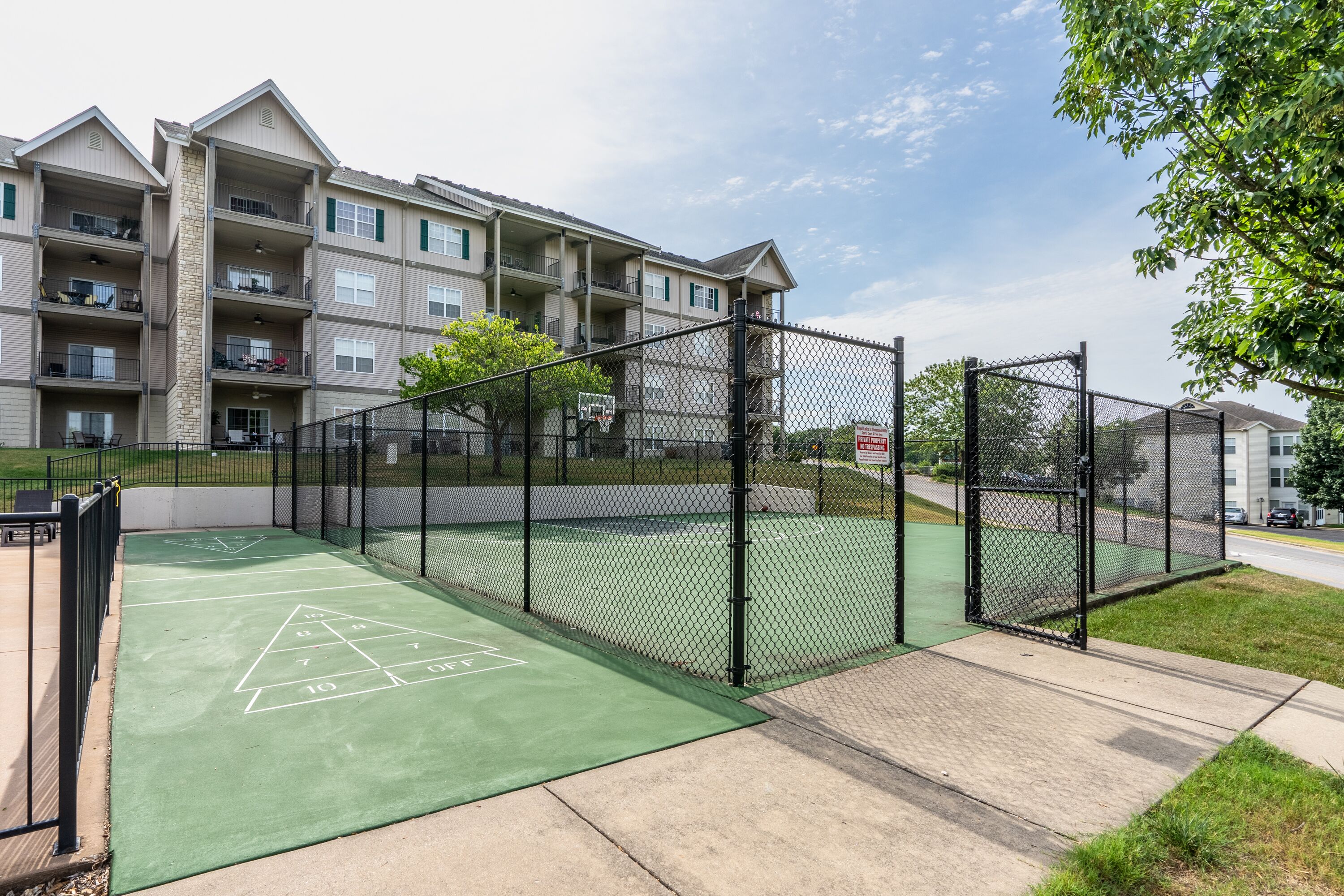 A tennis court with a green surface and a net, surrounded by a chain-link fence.