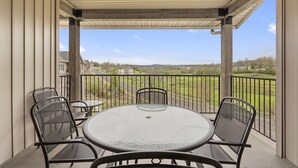 A covered balcony with a round table and four chairs, overlooking a residential area with houses and a road. - 2 King BR, 2BA Golf Condo - Private Balcony with View (Branson)