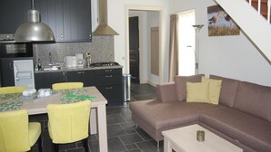 Une cuisine moderne avec des meubles de couleur sombre, une hotte de cuisine en acier inoxydable et un coin repas comprenant une table et des chaises.