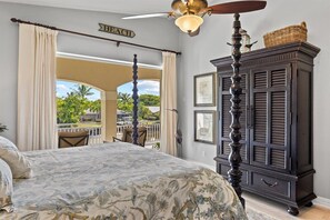 Un dormitorio con cama, ventilador de techo, un mueble de madera oscura y vistas al exterior.