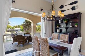 Un coin repas avec des chaises en osier, une table en bois, un lustre et un buffet en bois foncé agrémenté d’objets décoratifs.