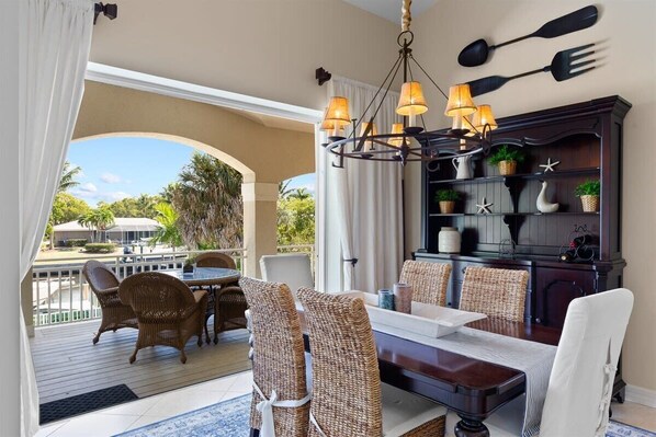 Un comedor con sillas de mimbre, una mesa de madera, una araña y un aparador de madera oscura con objetos decorativos.