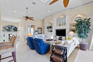 A spacious living room with a fireplace, blue sofas, a large potted plant, and a ceiling fan. - Waterfront Estate on Sanibel's East End with Integrated Pool and Spa Boat Dock (Sanibel)