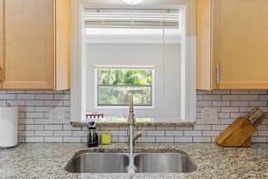 A kitchen with a stainless steel sink, a window with blinds, wooden cabinets, and a granite countertop.