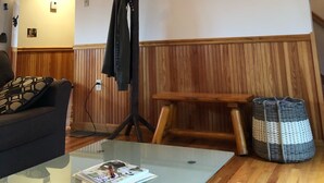 A cozy room with a sloped ceiling, wooden paneling, a coat rack, a bench, and a wicker basket. - Hideaway in the Great North Woods - direct access to snowmobile trails (Errol)