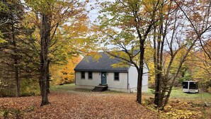 A small, single-story cabin with a front porch, surrounded by trees with autumn foliage. - Hideaway in the Great North Woods - direct access to snowmobile trails (Errol)