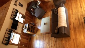 A spacious living room with a wooden floor, a grey sofa, a white coffee table, and a television mounted on the wall. - Hideaway in the Great North Woods - direct access to snowmobile trails (Errol)