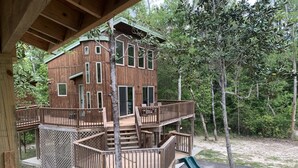 A multi-level wooden cabin with a deck and a slide, surrounded by trees. - Cozy Cabin on the River (D'Iberville)